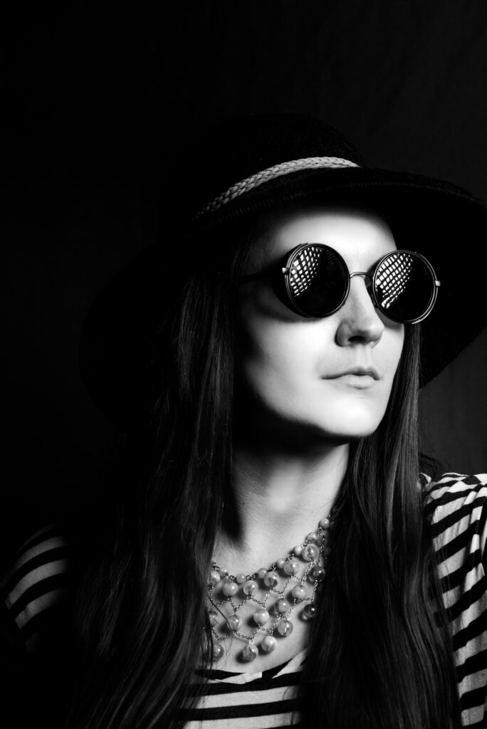 Black and white portrait of a woman wearing sunglasses and a hat, exuding fashion and elegance.