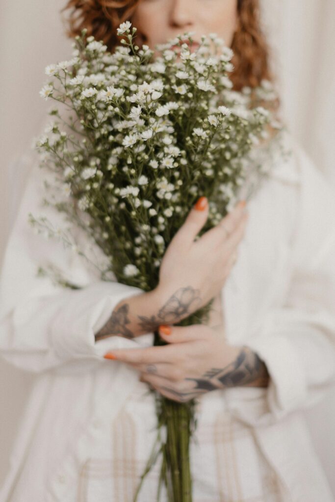 A woman with tattoos holds a bouquet of delicate white flowers indoors.