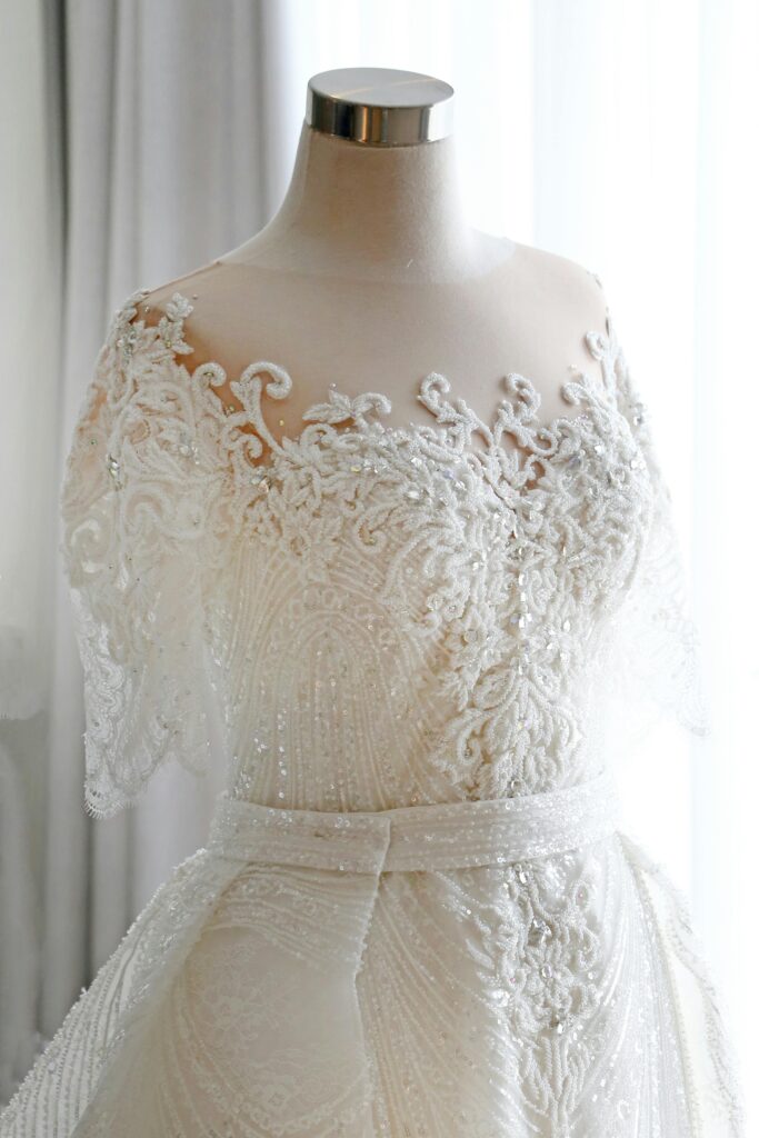 Intricately designed white lace wedding dress displayed on a mannequin with a soft, elegant atmosphere.