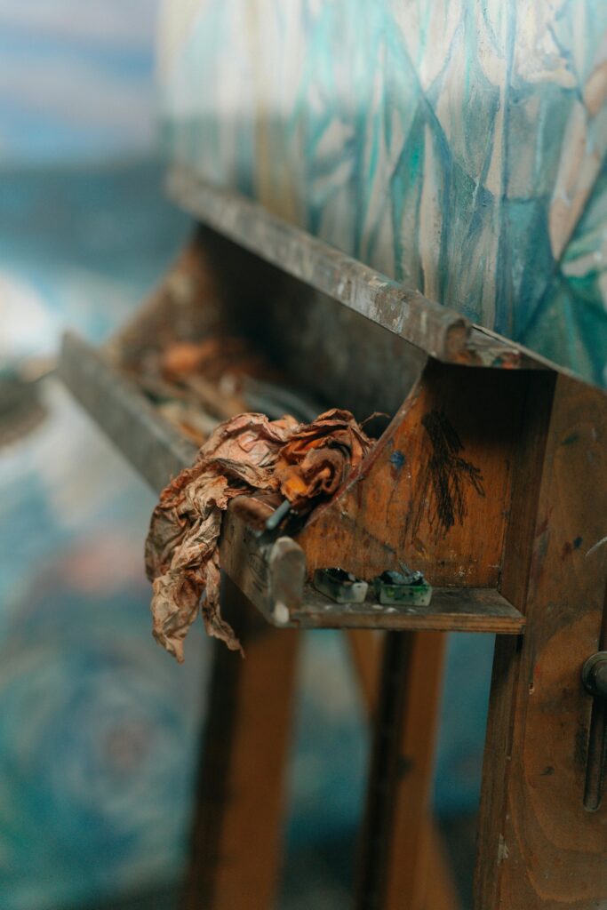 Close-up view of a wooden easel with a paint-splattered canvas and rags in an artist's studio.